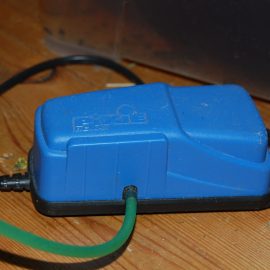Een blauwe aquariumluchtpomp met aangesloten luchtslang op een houten ondergrond.