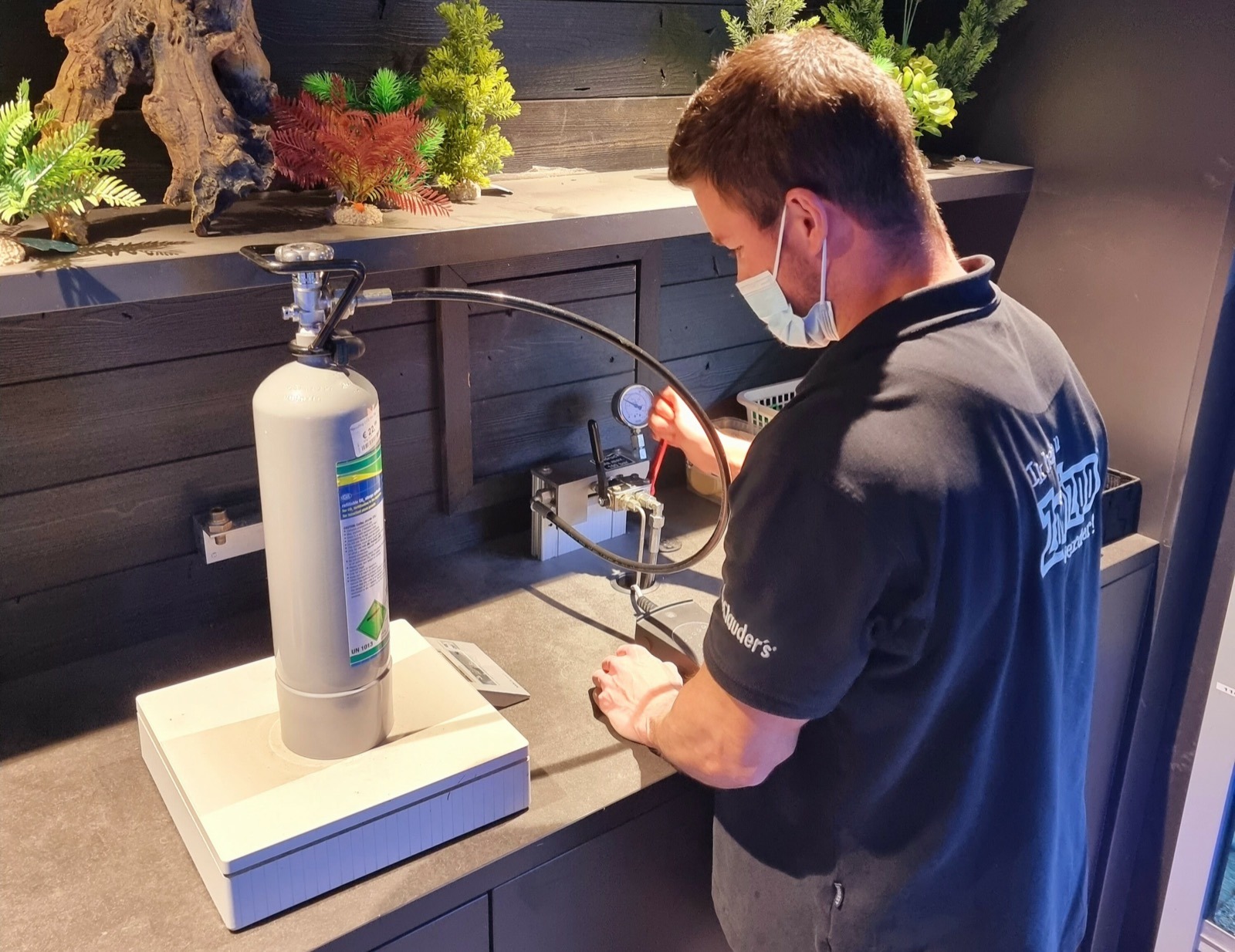 Een medewerker van Zowizoo vult een CO₂-fles bij aan het vulstation in de winkel, met de fles op een weegschaal.